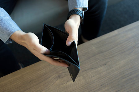 closeup empty wallet (no money) in the hands of an man with soft-focus and over light in the backgroundの写真素材