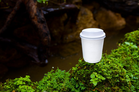 white paper cup of coffee in the beautiful nature with soft focus and over light in the background. mockup and templates to create greeting, cards, magazines, cover, poster and banners.の写真素材