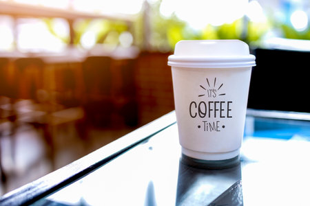 paper cup of coffee on table in cafe with soft-focus and over light in the backgroundの写真素材