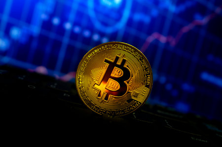 bitcoin gold coin on keyboard and chart with soft-focus and over light in the background....