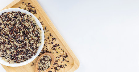 Closeup cooked brown rice blend in ceramic bowl, accompanied by wooden utensils and rice stalks on a...