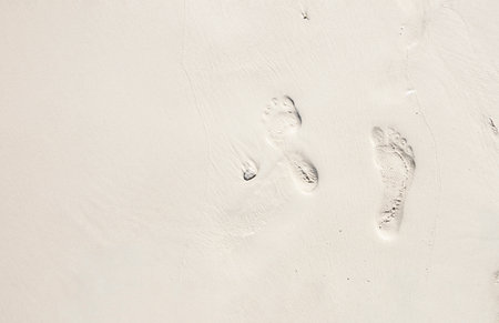 Fresh footprints on soft white sand, capturing a peaceful moment of a barefoot walk along the beach, symbolizing relaxation, travel, and serenityの写真素材