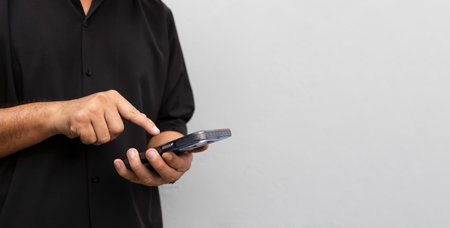Close-up of a man holding a smartphone, wearing a black shirt, using a mobile device for messaging,...