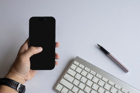 Person using smartphone at modern workspace with keyboard and pen on white background. Flat lay digital lifestyle concept for productivity.の写真素材