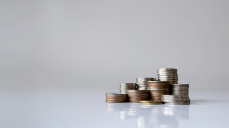 Piles of assorted coins arranged on white background symbolizing money, finance, saving, and economic growthの写真素材
