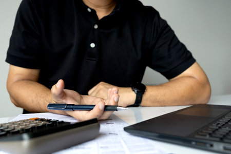 Businessman working on tax or finance report with laptop, calculator, and pen, focusing on financial...