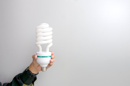 Minimalist concept image of a hand holding a spiral compact fluorescent light bulb (CFL),...