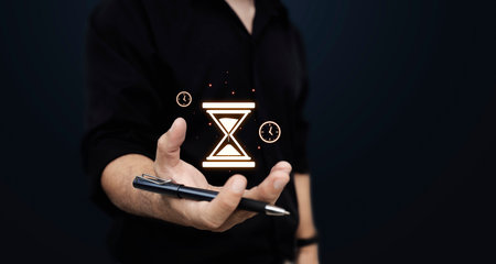 Man in black shirt holding glowing hourglass and clock hologram, symbolizing time management, deadline, productivity, and efficiency.の写真素材