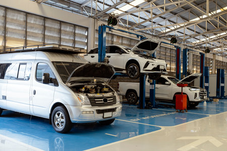 Electric and hybrid vehicles undergoing maintenance in professional auto repair workshop. Hydraulic lifts, diagnostic tools, and clean, well-lit garage environment.の写真素材