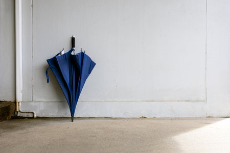 blue umbrella stands against a light concrete wall in a simple, minimalist scene with soft daylight and rainy dayの写真素材