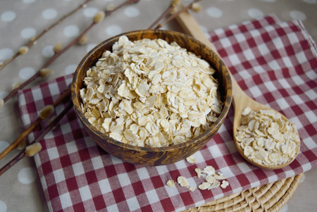 Raw Oat flakes in a wooden bowl with spoon on the table, healthy foodの写真素材
