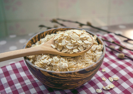Raw Oat flakes in a wooden bowl with spoon on the table, healthy foodの写真素材