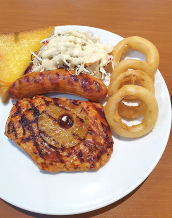 Grilled chicken, pineapple and sausages with sauce served with onion rings, salad and toast on a plate.の写真素材