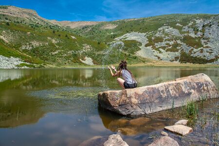 woman with dreadlocks throws water on a rock in a lake in the mountain