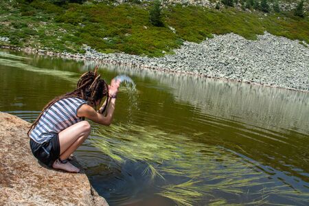 woman with dreadlocks throws water on a rock in a lake in the mountainの写真素材