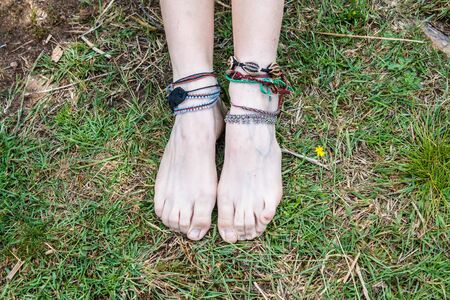 little feet of a girl with bracelets on the lawnの写真素材