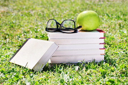 Books, glasses and apple on a meadowの写真素材