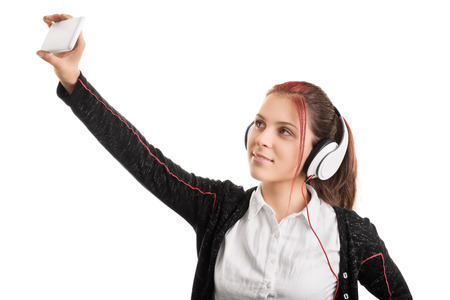 Young girl wearing headphones in school uniform and making a  selfie, isolated on white backgroundの写真素材
