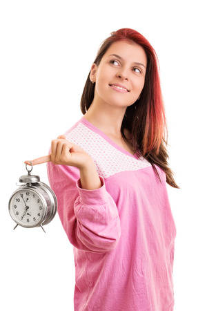 Wake up, its a beautiful day. Smiling young girl in pyjamas holding an alarm clock, isolated on white backgroundの写真素材