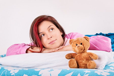 We're up with a smile on our faces. Young girl in her bed, awake with her teddy bear.の写真素材