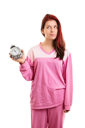 A portrait of a young girl in pyjamas holding an alarm clock, isolated on white background.の写真素材