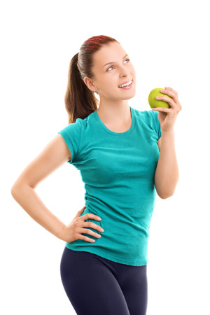 A portrait of a smiling young girl in fitness clothes holding an apple, isolated on white backgroundの写真素材