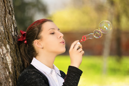 A portrait shot of a beautiful young girl in a park, making soap bubbles.の写真素材