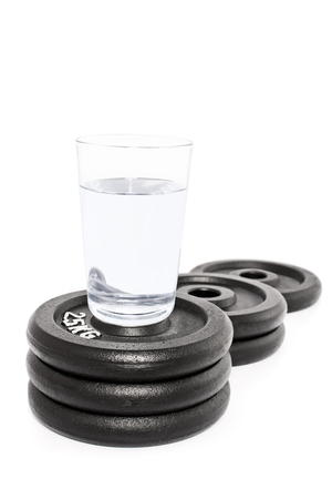 Glass of water put on a podium of weight plates, isolated on white background.の写真素材