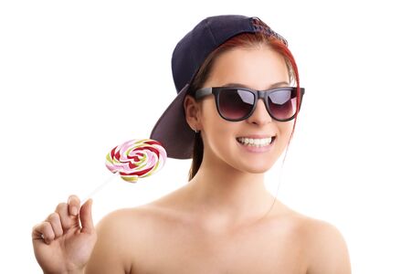 Cool beautiful girl with sunglasses and a snapback cap holding lollipop, isolated on a white background.の写真素材