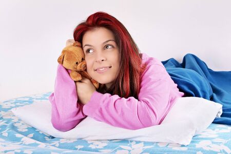 Young beautiful girl lying on the bed hugging a plush teddy bear, thinking of someone, isolated on a white background.の写真素材