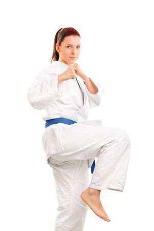 A portrait of a young girl in a kimono  with blue belt, preparing for a kick, isolated on white background.の写真素材