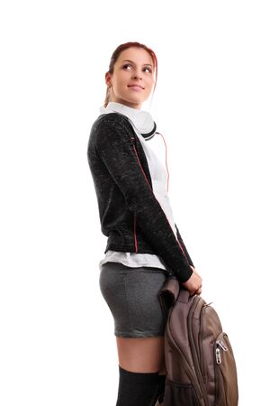 A portrait of a smiling female student in uniform with headphones, holding a backpack, isolated on white background. I can't wait to go back to school.の写真素材