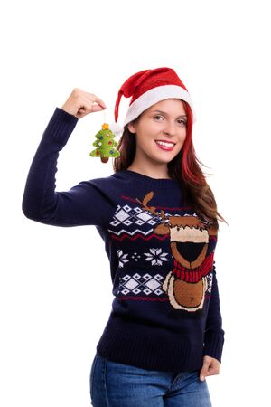 Beautiful smiling girl in a festive sweater with a Santa's hat on, holding a Christmas tree decoration, isolated on a white background.の写真素材