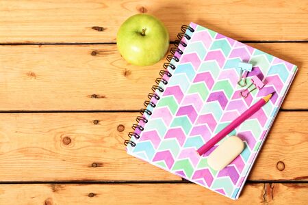 Top view of girly pink notebook with pencil, eraser, binder clips and apple on wooden background.の写真素材