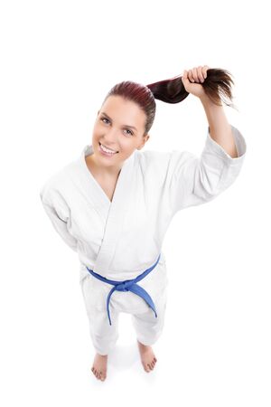 Top down view of a beautiful young smiling girl in a white kimono with blue belt holding her ponytail, isolated on white background.の写真素材