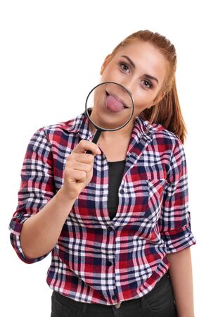Beautiful young woman showing her magnified tongue under magnifying glass. Portrait of a smiling young girl sticking her tongue out, looking at camera, isolated on white background.の写真素材
