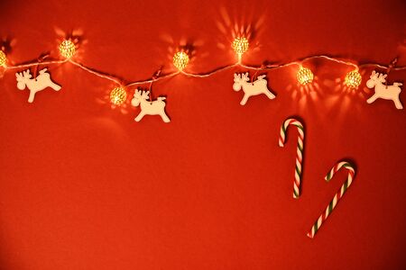 Christmas and New Year composition. Seasonal greeting card concept with white Christmas lights, reindeers and candy cane on red background. Christmas, winter, new year concept. Flat lay, top view, copy space. の写真素材