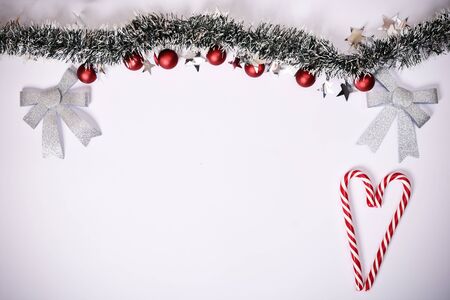 Christmas composition. Garland with red balls, stars, glittery bows and heart made of candy canes on white background. Christmas, winter, new year concept. Flat lay, top view, copy space.の写真素材