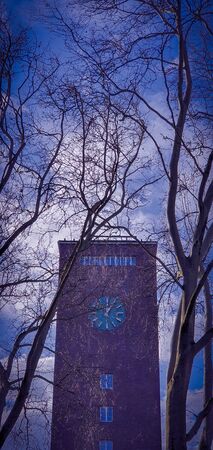 Red brick clock tower against clear blue sky and white clouds, seen through tree branches. Clock tower of the central train station in Oberhausen, Germany.の写真素材