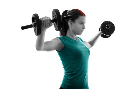 Fit attractive young woman working out with a set of dumbbells, backlit silhouette studio shot isolated on white background. Fitness and healthy lifestyle concept.の写真素材