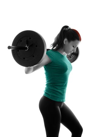 Fit attractive young woman working out with a barbell, looking down, backlit silhouette studio shot isolated on white background. Fitness and healthy lifestyle concept.の写真素材