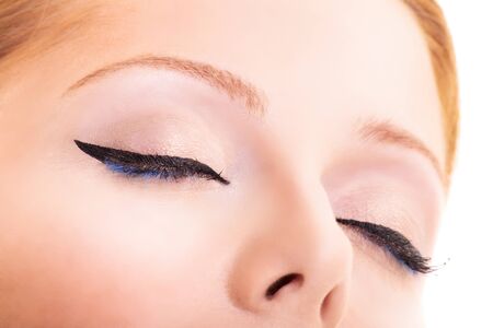 Close-up beauty shot of pretty young model with classic eyeliner, black and blue mascara, glowing clean skin and blond hair. Beauty and make up concept. Closeup macro shot of fashionable eyeliner on closed eyes.の写真素材