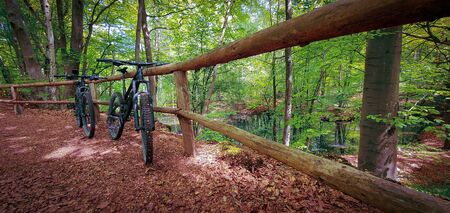 Two mountain bikes propped on a wooden fence next to a beautiful small lake on a green forest trail. Mountain biking concept. Freedom and recreation concept.の写真素材
