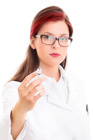 Close up of a young serious female doctor with glasses holding a syringe with needle, isolated on white background. Health care concept.の写真素材