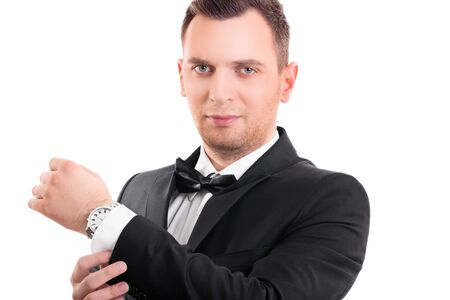 Portrait of a confident attractive young man in black suit with bow tie, adjusting the cufflinks on his white shirt, looking at the camera, isolated on a white background.の写真素材