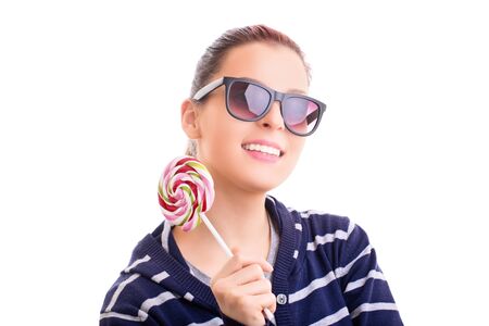 Beautiful young girl in casual clothes with sunglasses holding a colorful lollipop, isolated on white background.の写真素材