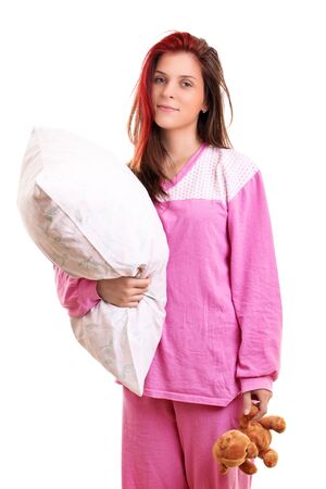 Beautiful smiling young girl in pink pajamas holding a pillow and a teddy bear, preparing to go to sleep, isolated on white background. Sleep and relaxation concept.の写真素材