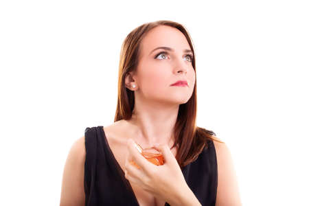 Beautiful young blond woman with elegant black dress applying perfume on herself, looking up, isolated on white background. Elegant woman putting on perfume. Elegance concept.の写真素材