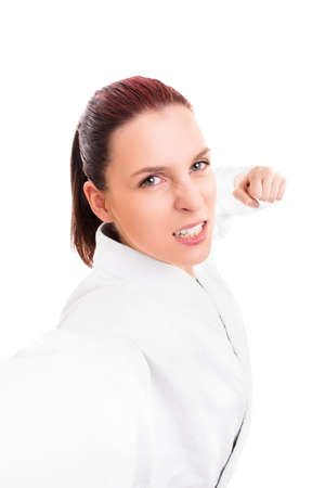 Close up portrait of a beautiful young girl in white kimono with the fists up punching the camera, isolated on white background. Martial art concept.の写真素材