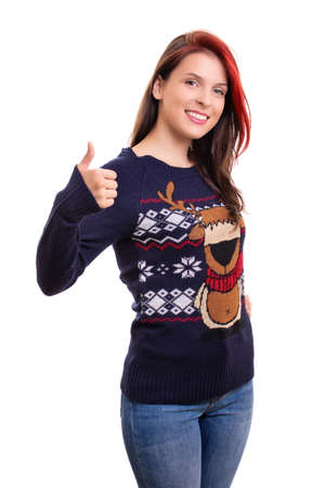 Beautiful smiling young girl in Christmas sweater showing thumb up gesture, isolated on white background. Christmas and New Year holiday concept.の写真素材